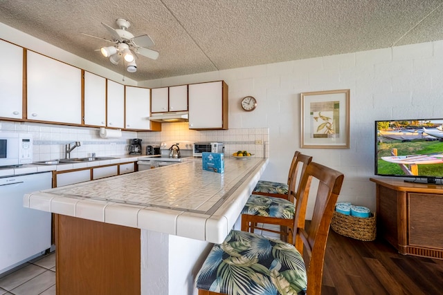 kitchen with white cabinets, sink, white appliances, a textured ceiling, and hardwood / wood-style flooring