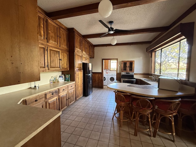 kitchen featuring black fridge, washer and dryer, ceiling fan, beamed ceiling, and range