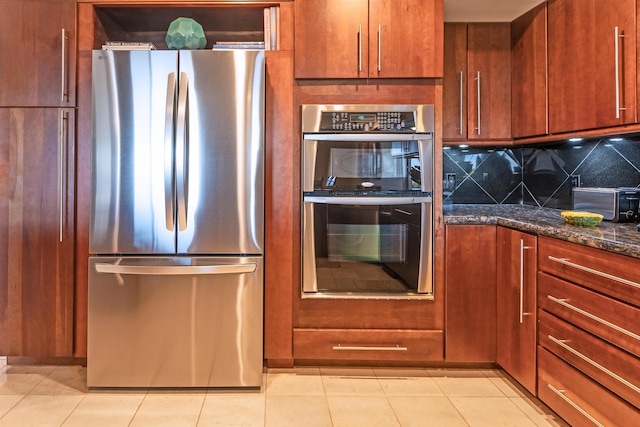 150 Puukolii Rd Unit 18, Lahaina, HI 96761 - kitchen with stainless steel appliances, decorative backsplash, brown cabinetry, dark stone counters, and light tile patterned floors