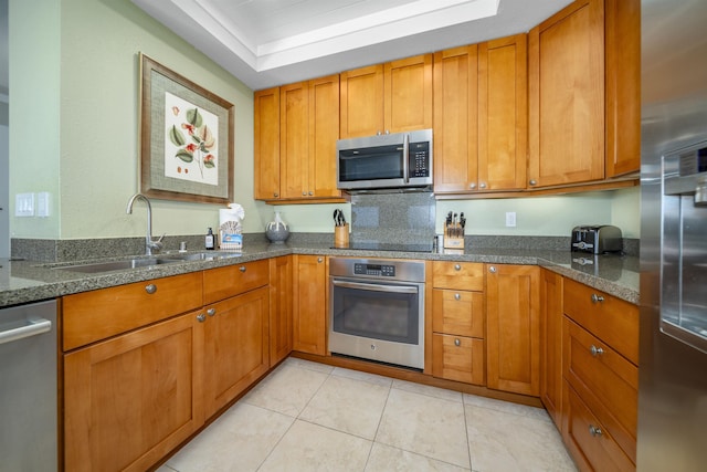 kitchen with light tile patterned flooring, dark stone countertops, sink, and appliances with stainless steel finishes