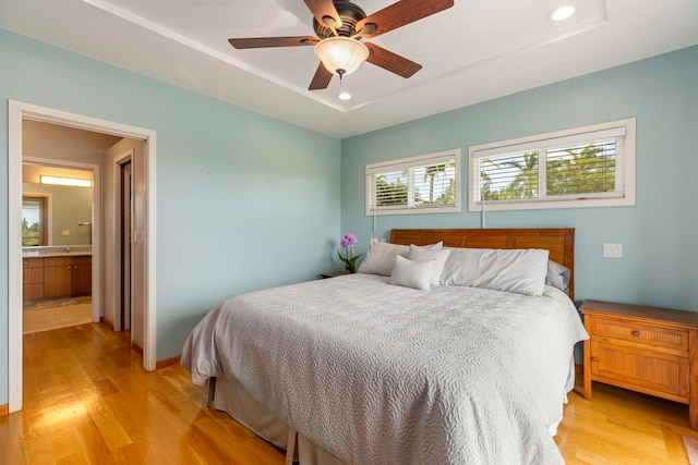 bedroom featuring connected bathroom, light hardwood / wood-style floors, a raised ceiling, and ceiling fan