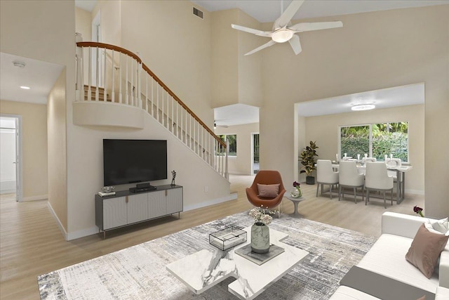 living room featuring a towering ceiling, light hardwood / wood-style flooring, and ceiling fan