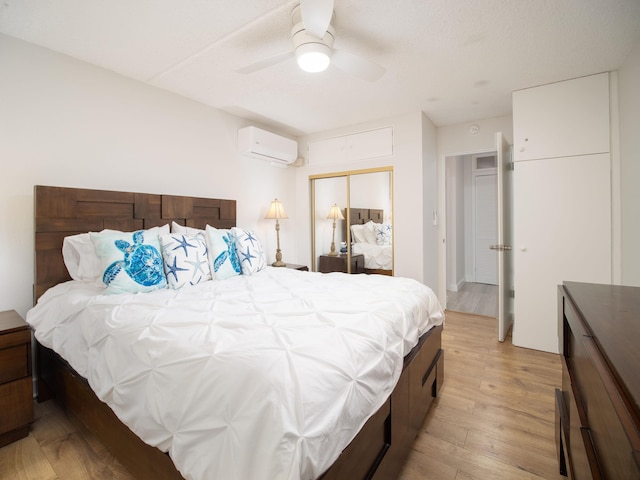 bedroom with an AC wall unit, a closet, ceiling fan, and light hardwood / wood-style flooring