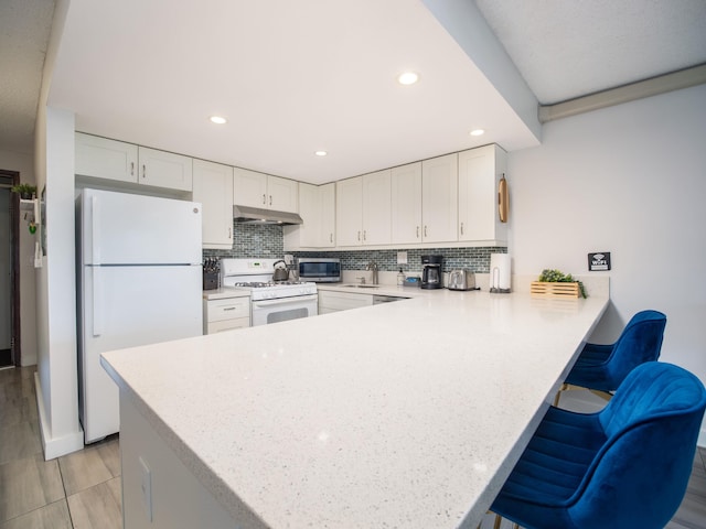 kitchen featuring kitchen peninsula, white appliances, sink, white cabinets, and a breakfast bar area