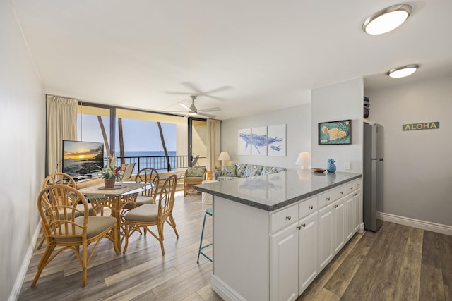 kitchen featuring wood-type flooring, a kitchen breakfast bar, white cabinets, floor to ceiling windows, and stainless steel fridge