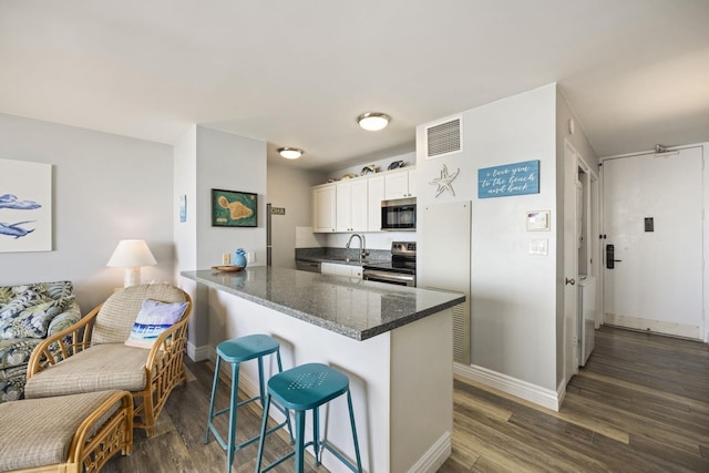 kitchen featuring white cabinetry, stainless steel appliances, dark hardwood / wood-style floors, kitchen peninsula, and a breakfast bar