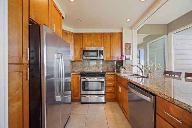 kitchen with backsplash, appliances with stainless steel finishes, light tile patterned floors, light stone countertops, and sink