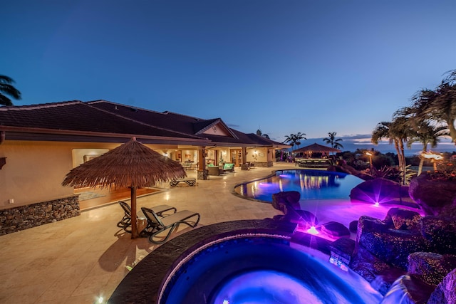 pool at dusk with an in ground hot tub and a patio