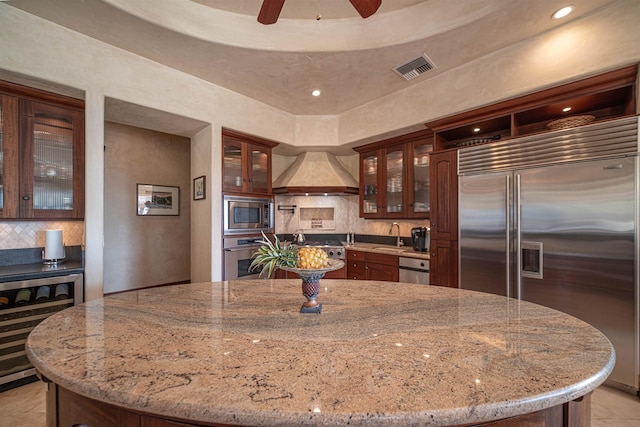 kitchen featuring built in appliances, a kitchen island, light stone countertops, and custom range hood