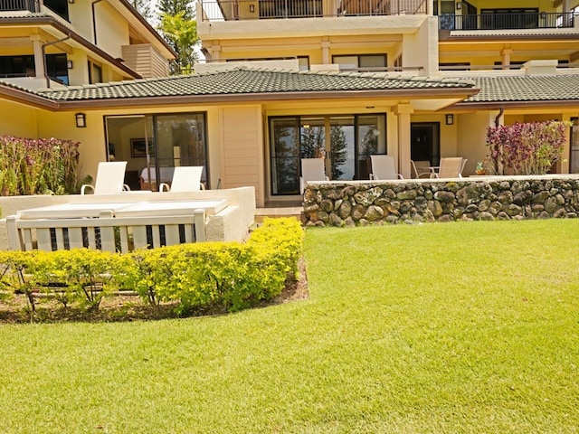 rear view of property featuring a balcony and a lawn