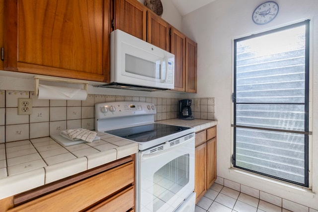 kitchen featuring tile counters, tasteful backsplash, lofted ceiling, white appliances, and light tile patterned floors