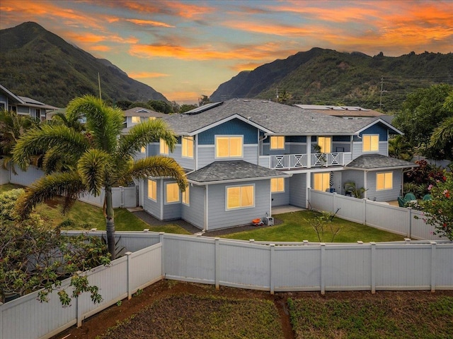 traditional home featuring a front yard, a fenced backyard, a mountain view, solar panels, and a balcony