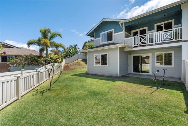 rear view of property featuring a lawn, a balcony, and a fenced backyard