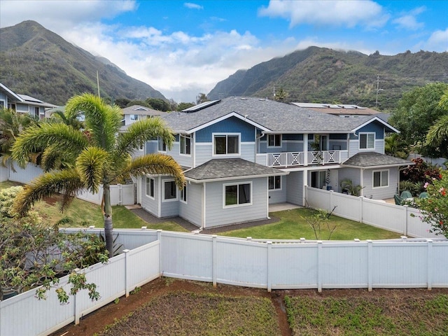 view of front of property featuring a balcony, a front yard, a fenced backyard, roof with shingles, and a mountain view