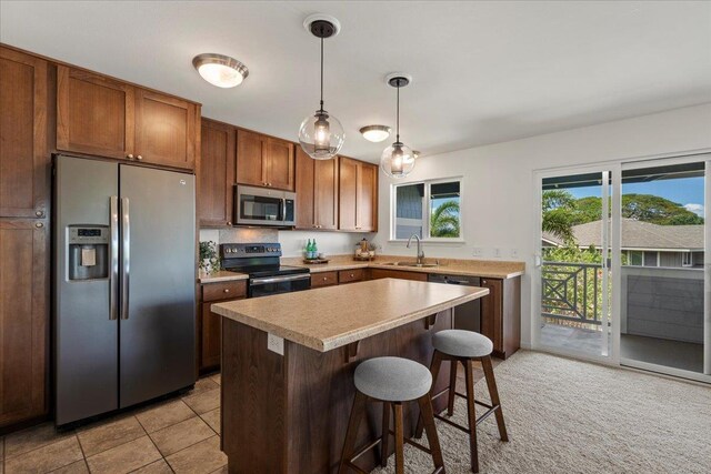 kitchen featuring a kitchen island, a breakfast bar, light countertops, appliances with stainless steel finishes, and decorative light fixtures