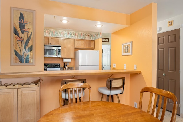 kitchen featuring light tile patterned floors, a breakfast bar area, stove, and white refrigerator