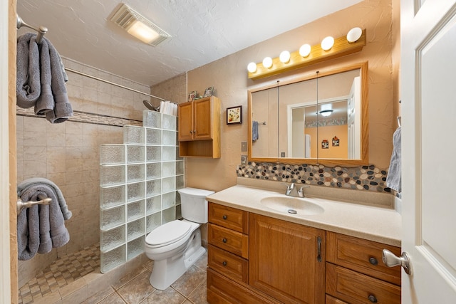 bathroom with tile patterned flooring, toilet, a tile shower, and vanity