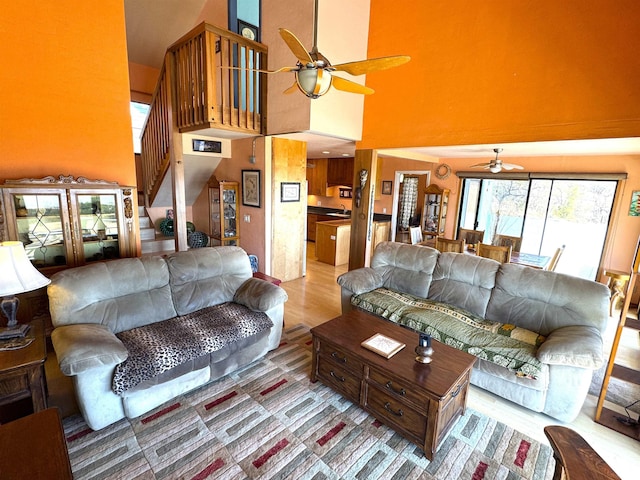 living room featuring ceiling fan, a high ceiling, and light wood-type flooring