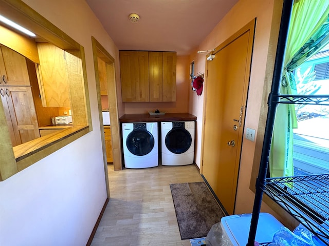 clothes washing area with cabinets, independent washer and dryer, and light hardwood / wood-style flooring