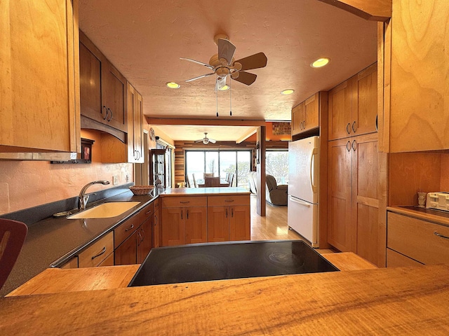 kitchen featuring ceiling fan, sink, kitchen peninsula, white fridge, and black electric stovetop