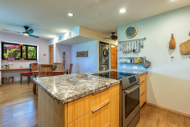 kitchen with stacked washer / dryer, light hardwood / wood-style floors, kitchen peninsula, stainless steel range with electric stovetop, and stone counters