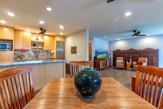 kitchen with dark wood-type flooring, stainless steel appliances, light brown cabinetry, decorative backsplash, and light stone counters