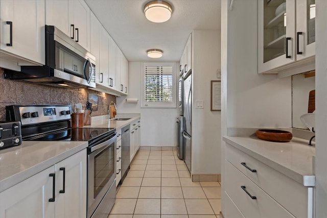 kitchen with appliances with stainless steel finishes, tasteful backsplash, white cabinetry, light tile floors, and sink