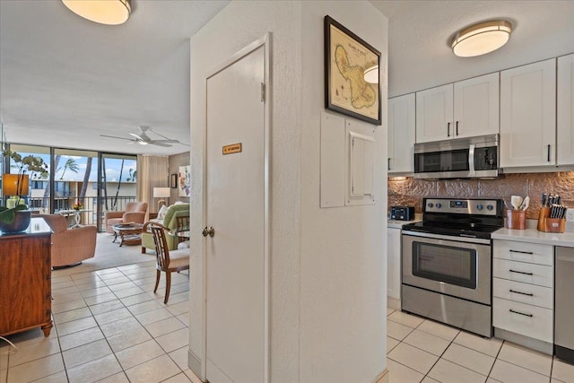 kitchen with tasteful backsplash, white cabinetry, stainless steel appliances, a wall of windows, and ceiling fan