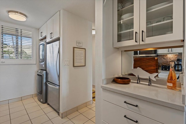 kitchen featuring white cabinets, stacked washer / drying machine, appliances with stainless steel finishes, and light tile flooring