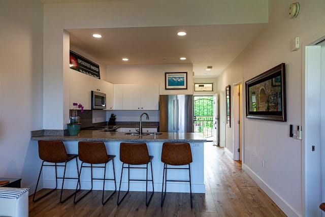 kitchen with wood finished floors, a peninsula, a sink, stainless steel appliances, and white cabinets