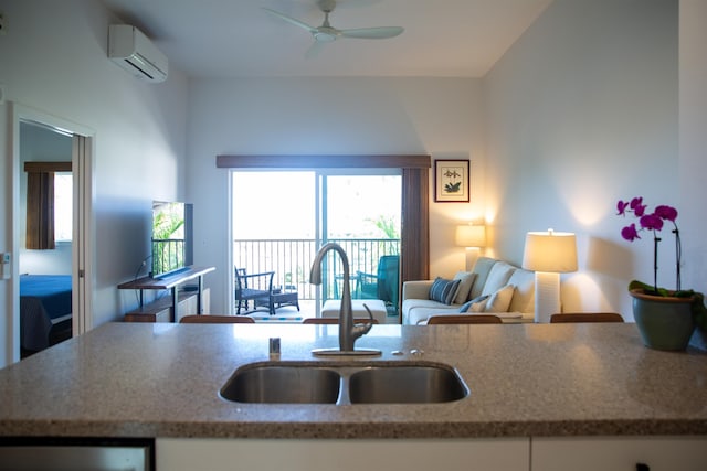 kitchen with light stone counters, a sink, an AC wall unit, white cabinetry, and open floor plan