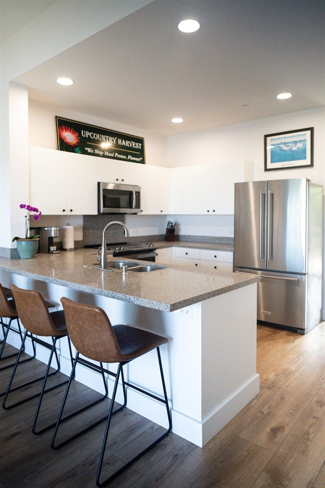 kitchen with appliances with stainless steel finishes, a peninsula, wood finished floors, white cabinetry, and a sink