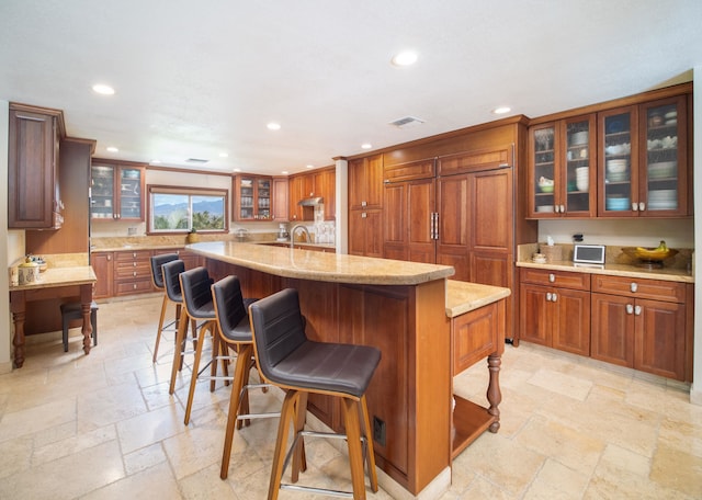 kitchen with a kitchen breakfast bar, a kitchen island with sink, and light stone counters