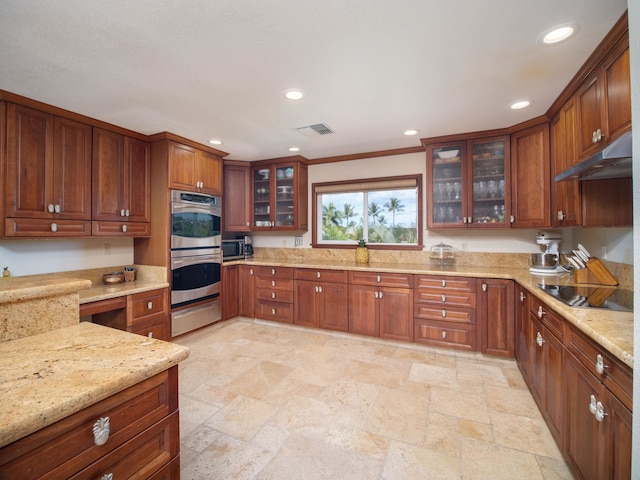 kitchen with black electric stovetop, double oven, light stone counters, and crown molding