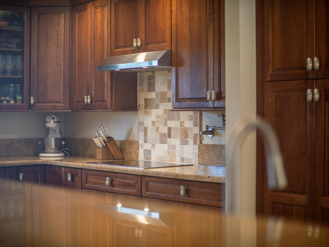 kitchen featuring black electric stovetop, light stone counters, and backsplash