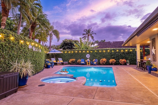 pool at dusk featuring an in ground hot tub and a patio area