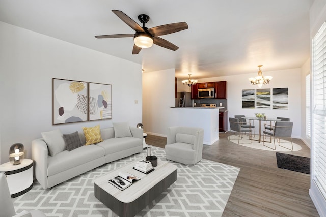 living room featuring ceiling fan with notable chandelier and light hardwood / wood-style flooring