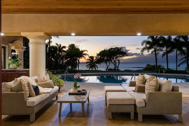 patio terrace at dusk featuring pool water feature, a water view, and an outdoor living space