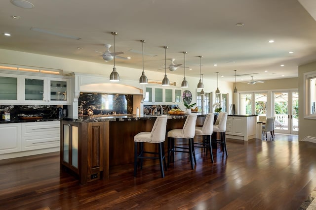 kitchen with tasteful backsplash, white cabinets, hanging light fixtures, ceiling fan, and a spacious island