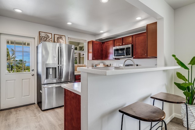 kitchen with a kitchen bar, kitchen peninsula, stainless steel appliances, and light hardwood / wood-style floors