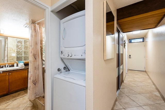 laundry area with light tile patterned floors, a textured ceiling, stacked washing maching and dryer, and sink