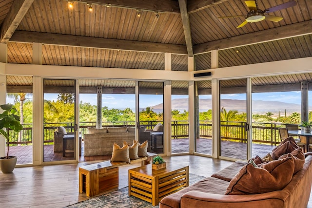 sunroom / solarium with a mountain view, lofted ceiling with beams, wooden ceiling, and ceiling fan