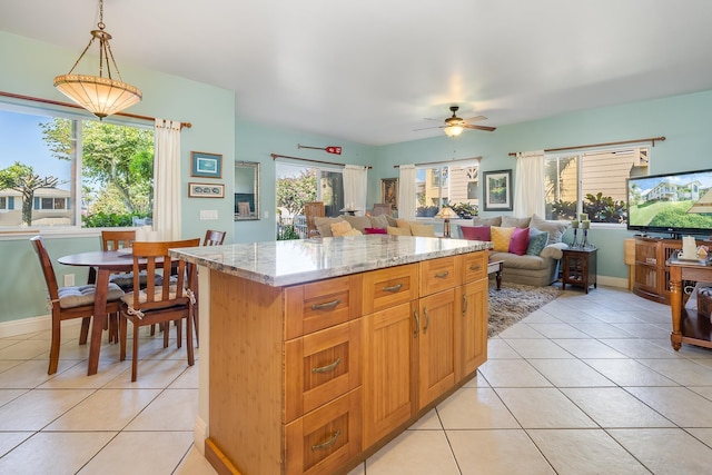 kitchen with pendant lighting, a center island, ceiling fan, light tile patterned floors, and light stone counters