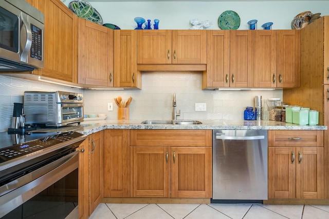 kitchen with light stone countertops, sink, backsplash, light tile patterned flooring, and appliances with stainless steel finishes