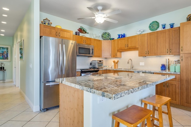 kitchen featuring sink, stainless steel appliances, light tile patterned floors, a breakfast bar area, and a kitchen island