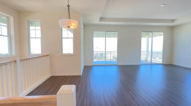 unfurnished room with dark wood-style floors, a tray ceiling, baseboards, and a wealth of natural light