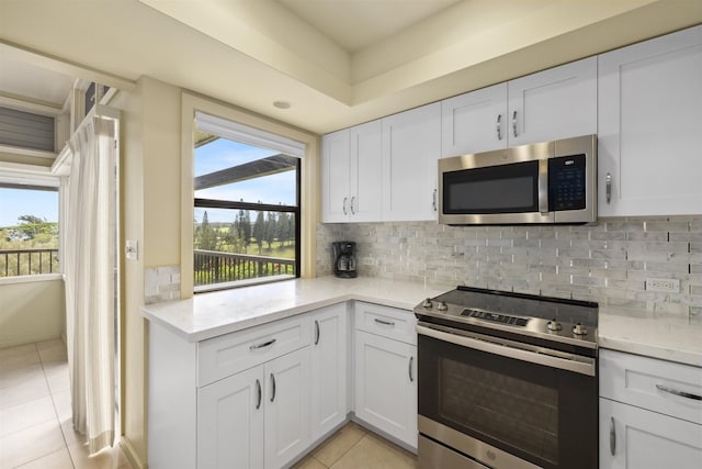 kitchen featuring white cabinets, stainless steel appliances, backsplash, light stone counters, and light tile patterned floors