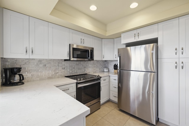 kitchen with appliances with stainless steel finishes, white cabinets, backsplash, light stone counters, and light tile patterned flooring