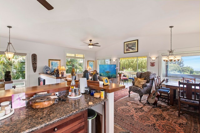 kitchen featuring ceiling fan, hanging light fixtures, vaulted ceiling, and dark stone countertops