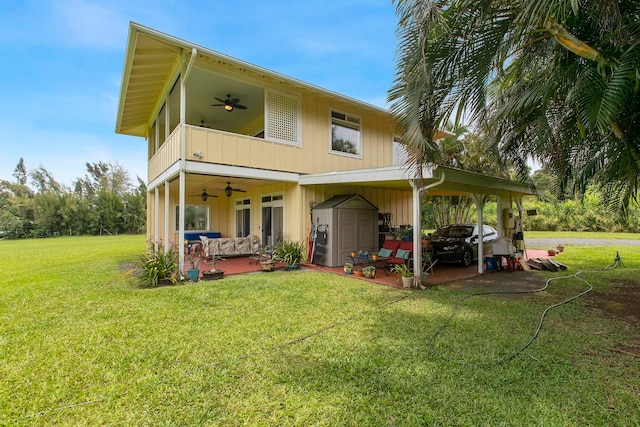 back of house featuring a storage shed, ceiling fan, a carport, and a lawn